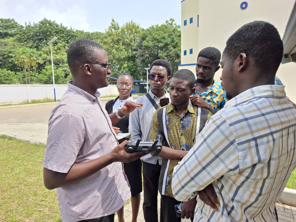 Drone instructor, Kwadwo, explaining the techniques for flying drones to graduate students, standing outside of the building 
