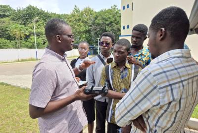 Drone instructor, Kwadwo, explaining the techniques for flying drones to graduate students, standing outside of the building 